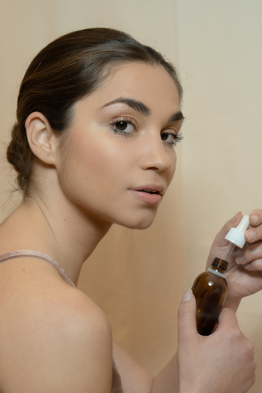 Photo of a Woman Holding a Brown Bottle and a White Dropper